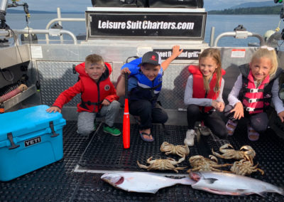 kids posing with caught salmon and crabs on the boat deck